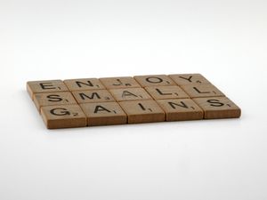 Close-up of Scrabble tiles forming the phrase 'Enjoy Small Gains', signifying the importance of realizing that small steps lead up to big results.