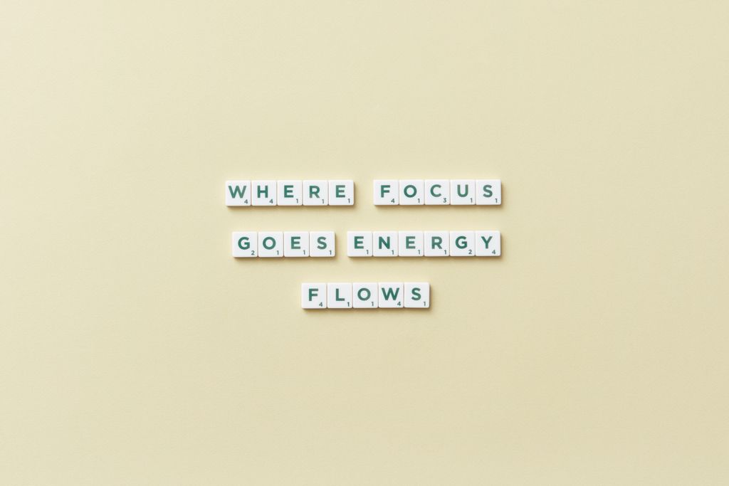Inspirational Mindfulness quote, 'Where Focus Goes Energy Flows' spelled with Scrabble tiles on a minimalist background.