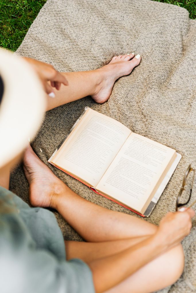 Woman being in the present moment while sitting on a blanket reading outdoors, enjoying a leisurely picnic.